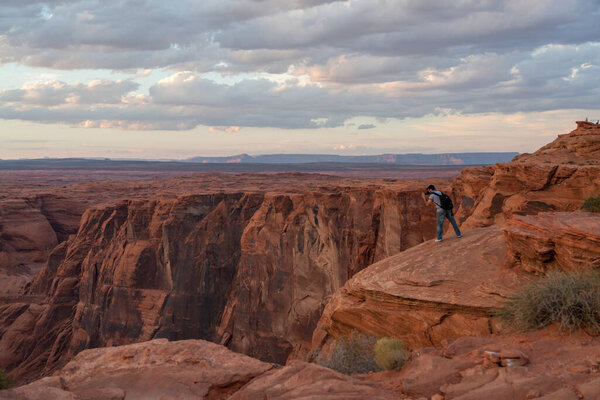 Horseshoe Bend, Arizona / USA - October 25, 2014:  A man stands of the edge of a cliff at Horseshoe Bend near Page, Arizona at sunset to take pictures of the Colorado River below.