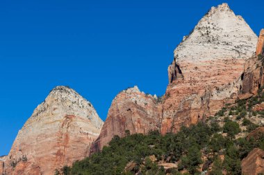 Kırmızı, turuncu ve beyaz kumtaşı katmanlı yüksek dramatik uçurumlar ve Utah, Zion Ulusal Parkı 'nda açık mavi bir gökyüzü..