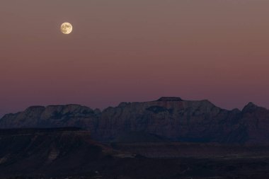 Dolunay, Zion Ulusal Parkı 'nın dramatik dağlarında alacakaranlıkta, yumuşak pembe gökyüzü ile yükseliyor..