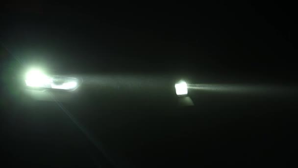 Машина светит фарами ночью под легким дождем — стоковое видео