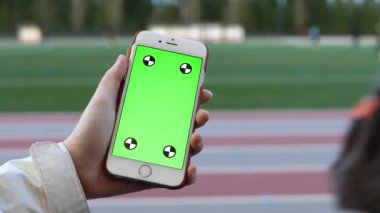 Kadın yeşil bir ekran ile boş bir akıllı aygıt under sport adlı tutar.