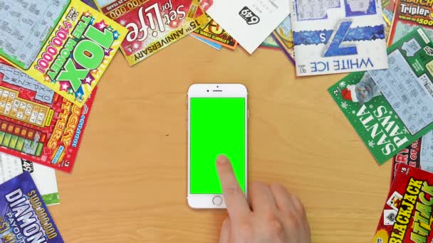 Tiro superior do homem usando iphone com vários gestos de mão na tela verde com vários bilhetes de loteria e arranhões na mesa — Vídeo de Stock