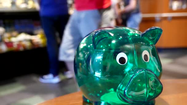 Hand plaatsen van munten op groene spaarpot in Starbucks winkel — Stockvideo