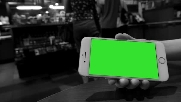 Hand hält grünes Bildschirm-iPhone im Starbucks-Geschäft mit schwarz-weiß getöntem Hintergrund — Stockvideo