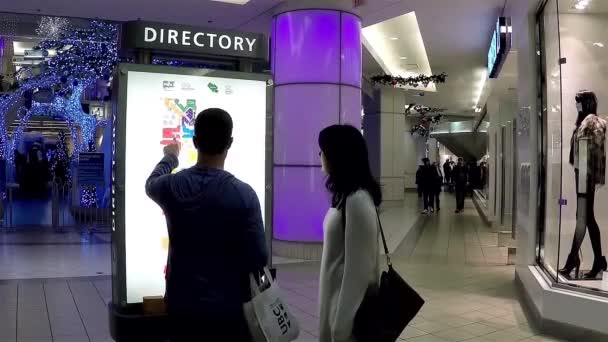 Casal verificar a posição da loja na frente do diretório sinal dentro shopping center — Vídeo de Stock