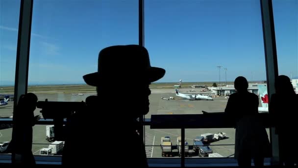 Silhouette of people close up looks through window at planes with tracking motion — Stock Video