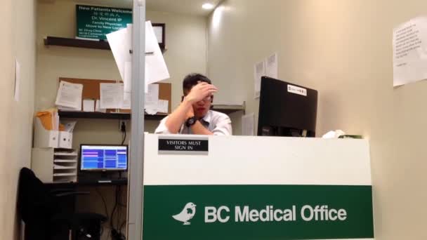 Young man at work as receptionist inside BC medicial office — Stock Video