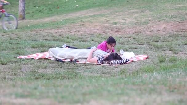 Mother and daughter lying down on the grass in the park — Stock Video