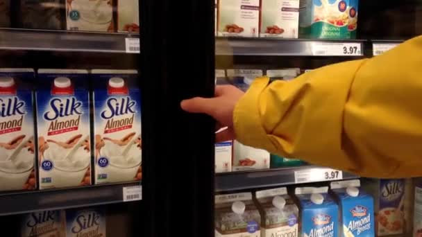 Mujer seleccionando leche de almendras en la tienda de comestibles departamento de lácteos y congelados . — Vídeo de stock