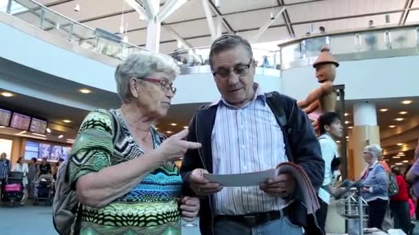 Primer plano de una pareja de ancianos leyendo la recuperación de información en el vestíbulo de llegada internacional — Vídeo de stock