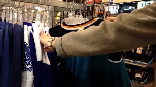 Женщина выбирает одну из спортивных рубашек — стоковое видео