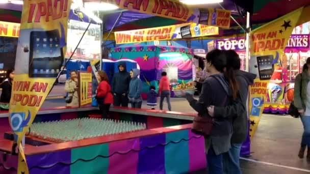 Pareja comiendo papas fritas y viendo a la gente lanzar anillos sobre la botella juego — Vídeo de stock