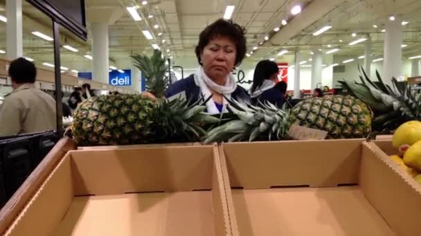 Woman selecting sweet pineapple in grocery store produce department. — Stock Video