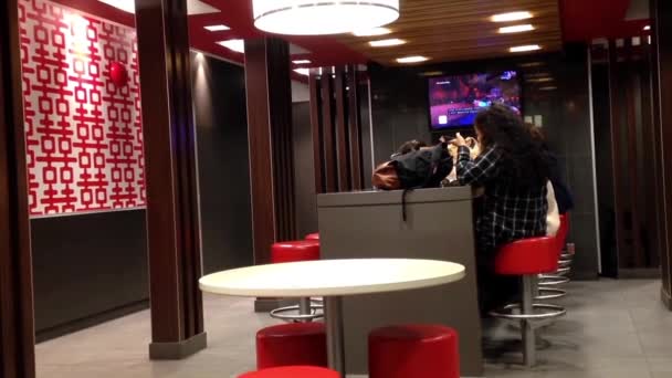 Люди едят еду и смотрят телевизор в ресторане быстрого питания mcdonalds — стоковое видео