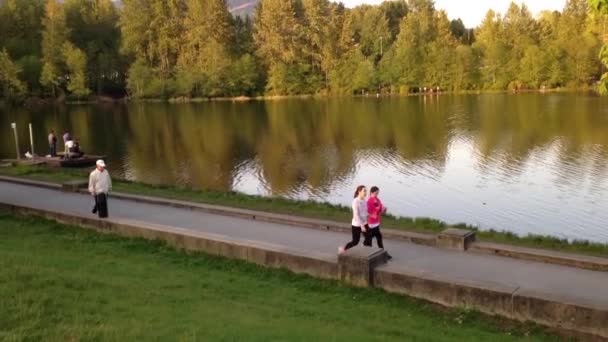 Ludzie chodzą w parku nad jeziorem w ciągu dnia — Wideo stockowe