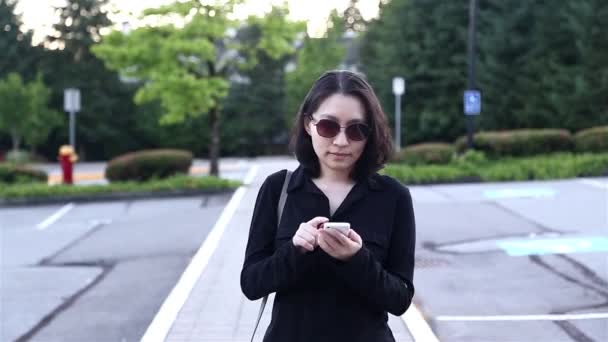 Mujer asiática que usa gafas de sol y lee el mensaje del teléfono móvil en el estacionamiento — Vídeo de stock