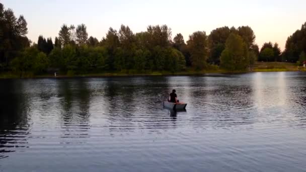 A man with his son in a small canoe across the calm waters of Coquitlam lake. — Stock Video