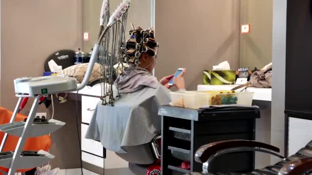 Femme ayant une permanente et la recherche photo sur téléphone portable dans un salon de coiffure — Video