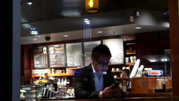 Shotting vanuit buiten raam van klant kopen van koffie en mobiel bericht bij Starbucks controleren — Stockvideo