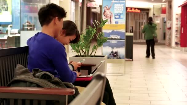 Pareja jugando a la computadora y el teléfono celular en el área de descanso dentro del centro comercial — Vídeos de Stock