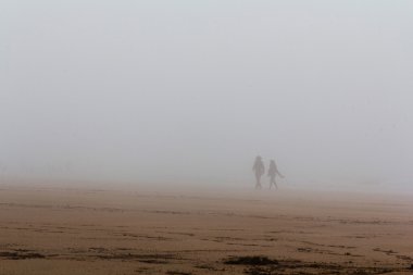İnsanlar bir sis kaplı plaj boyunca yürüyüş