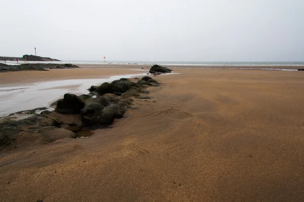 Мокрий пісок і скелі на пляжі — стокове фото