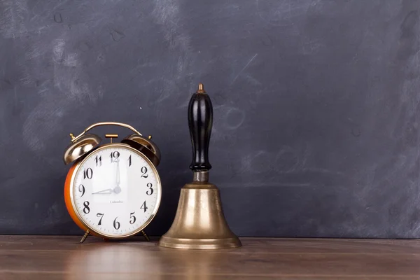 Bell and alarm clock against a blackboard — Stock Photo, Image