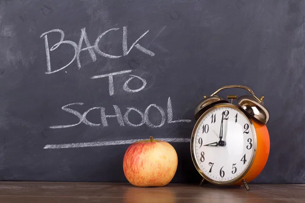 Clock and an apple against a blackboard