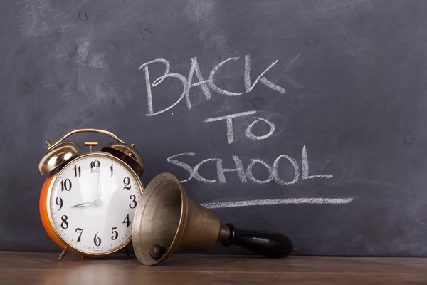 Klok en wekker tegen een schoolbord — Stockfoto