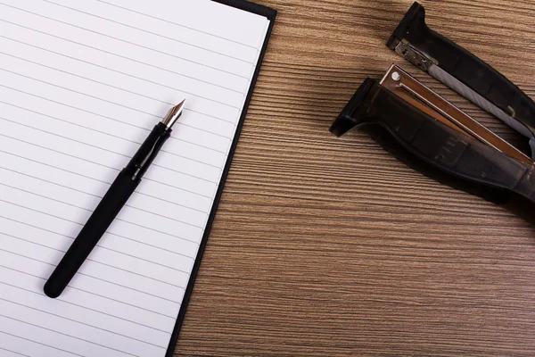 Lay flat image of a notebook and stapler on a wooden surface — Stock Photo, Image