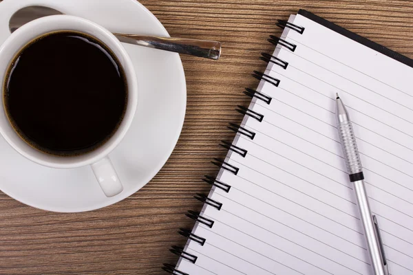 Cup of black coffee and notebook on wooden surface — Stock Photo, Image