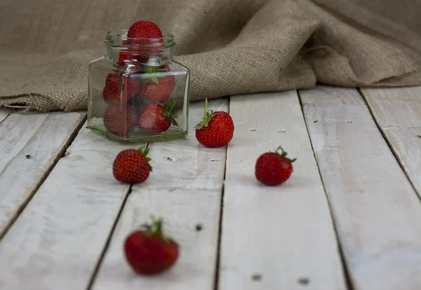 Fresas en un frasco y derramadas en la mesa — Foto de Stock