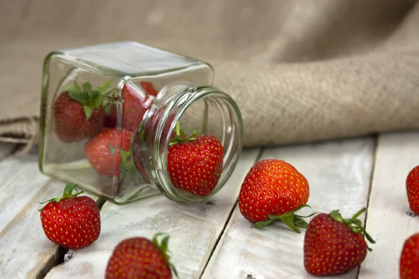Fresas en un frasco y derramadas en la mesa — Foto de Stock