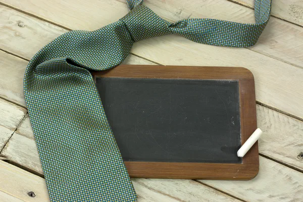 Tie and blackboard on wooden background — Stock Photo, Image