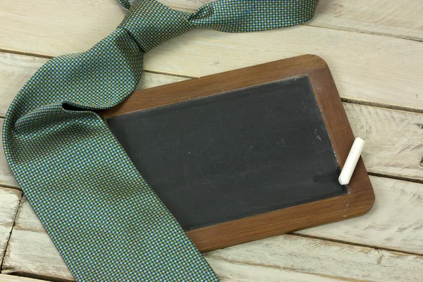 Tie and blackboard on wooden background — Stock Photo, Image