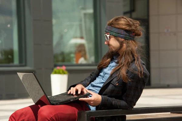Young hipsters with the computer sits on a bench. — Stock fotografie