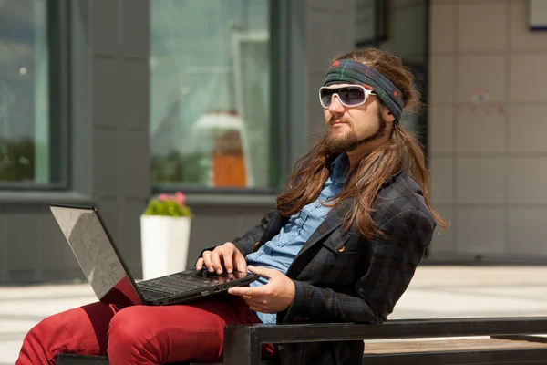 Young hipsters with the computer sits on a bench. — Stock fotografie