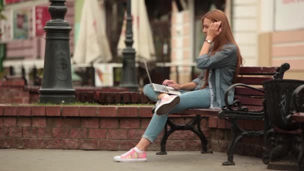 Dívka pracující na počítači na ulici a zvedne telefon. — Stock video