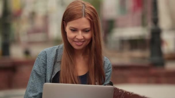 Ze communiceert in sociale netwerken en de glimlach op straat met een laptop. — Stockvideo