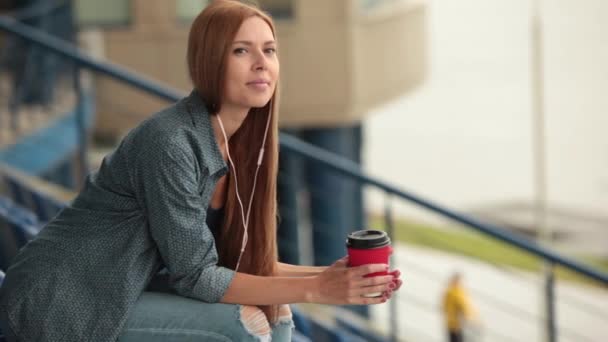Jovem linda menina bonita sentada na rua com uma xícara de café . — Vídeo de Stock