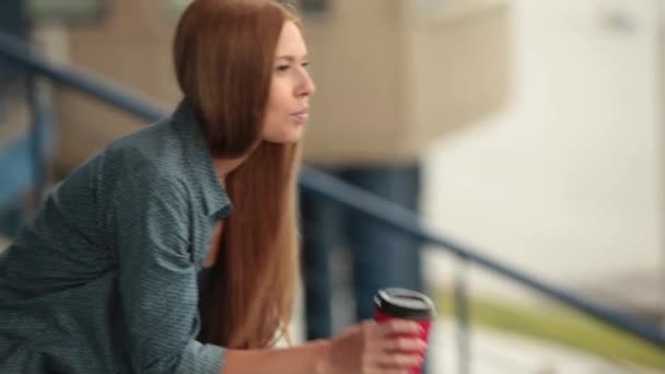 Młoda piękna dziewczyna siedzi z filiżanką kawy i rozmawia przez telefon. — Wideo stockowe