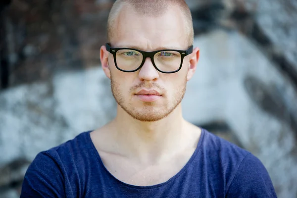 Porträt des jungen Mannes mit Brille vor dem Hintergrund einer Betonwand mit Graffiti. der Kerl schaut in die Kamera. — Stockfoto