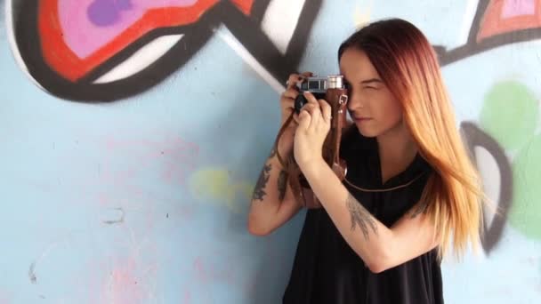 Ragazza con fotocamera vintage contro il muro graffiti e fotografie . — Video Stock