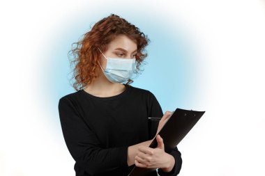 Yüzünde defter ve elinde kalemle koruyucu bir maske olan genç bir kız beyaz arka plana izole edilmiş metni yazar.,