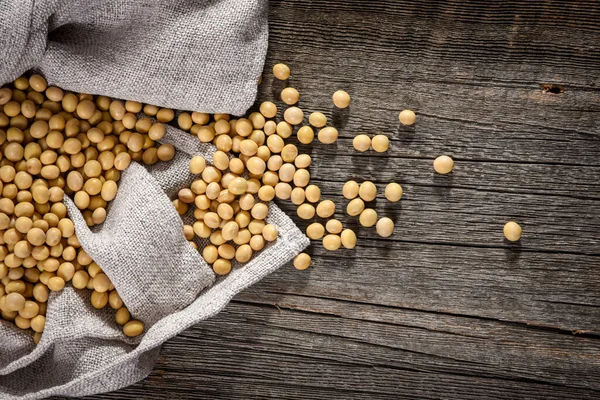 Close-up of soybean on wood background in jute sack. — Stock Photo, Image