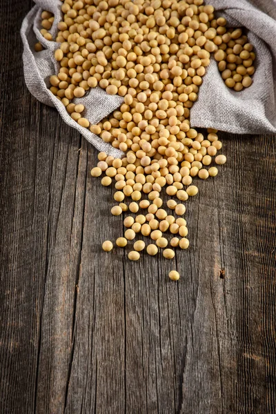 Close-up of soybean on wood background in jute sack. — Stock Photo, Image