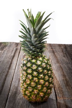 Beyaz arka planda ahşap bir tahtada yaprakları olan büyük bir ananas.