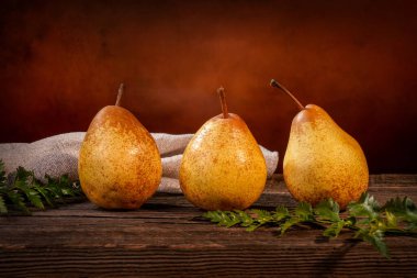 Üç sarı armut ve bir eğreltiotu bir ahır ahşap masa üzerinde bir fon önünde