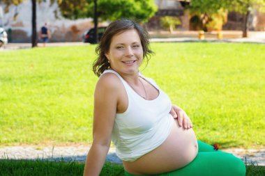 Doğadaki hamile karnını kapatır güneşli bir günde yeşil bir çayırda oturur.