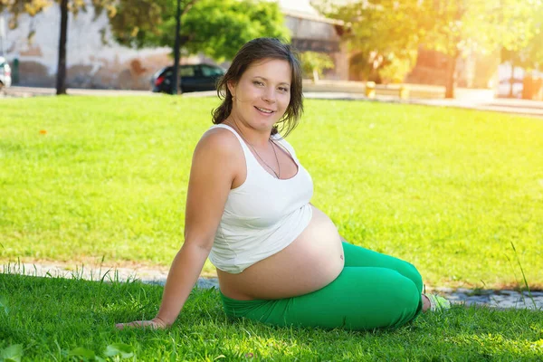 Doğadaki hamile karnını kapatır güneşli bir günde yeşil bir çayırda oturur.